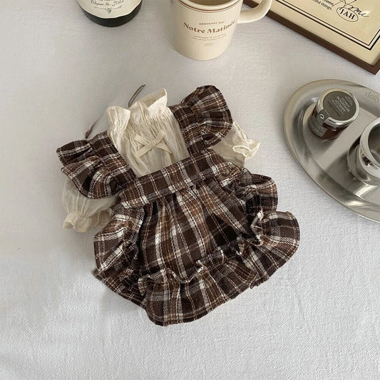 Plaid dress with ruffles on a white surface with a coffee cup and saucer in the background.