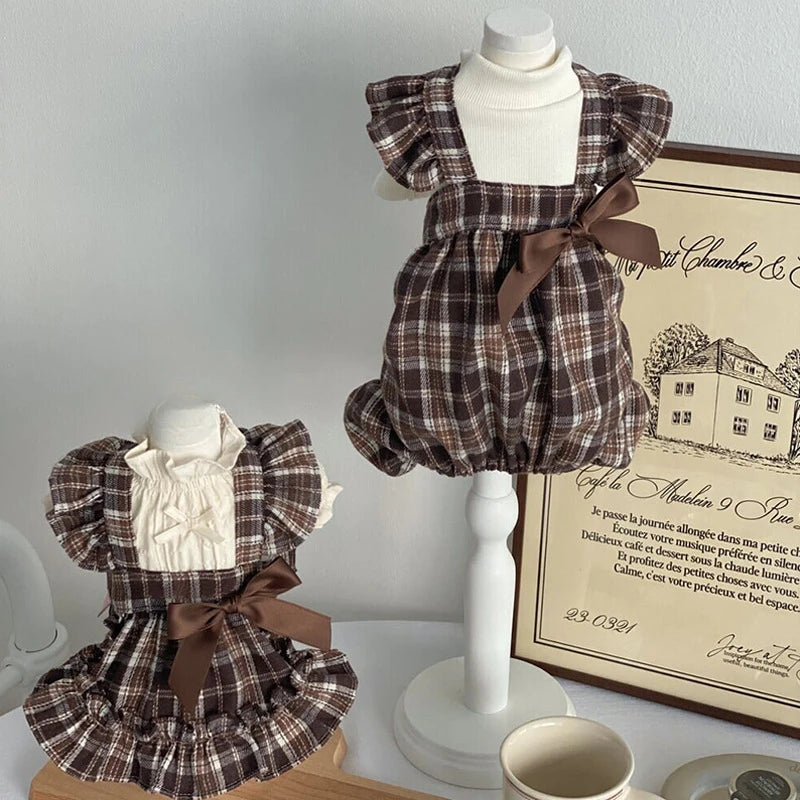 Two plaid rompers on mannequins with a framed document in the background.
